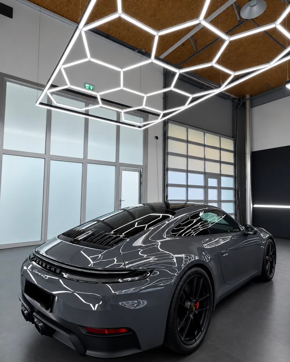 Dunkelgrauer Porsche 911 Carrera 4S von schräg hinten in der Werkstatt; auf Heckdeckel und Flanke stehen die Wabenleuchten als klare Linien.